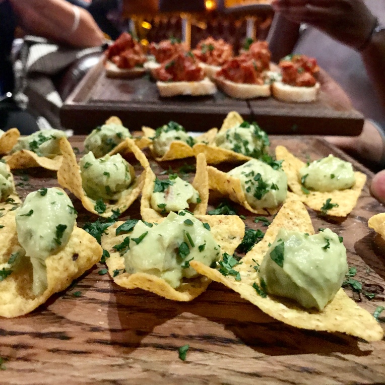 A board of mini tomato and toast on the far side and nachos with dip closer to the picture